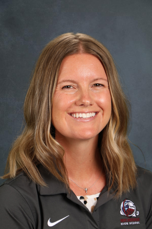Smiling woman with long, wavy hair, wearing a gray polo shirt with a school logo, against a dark background.